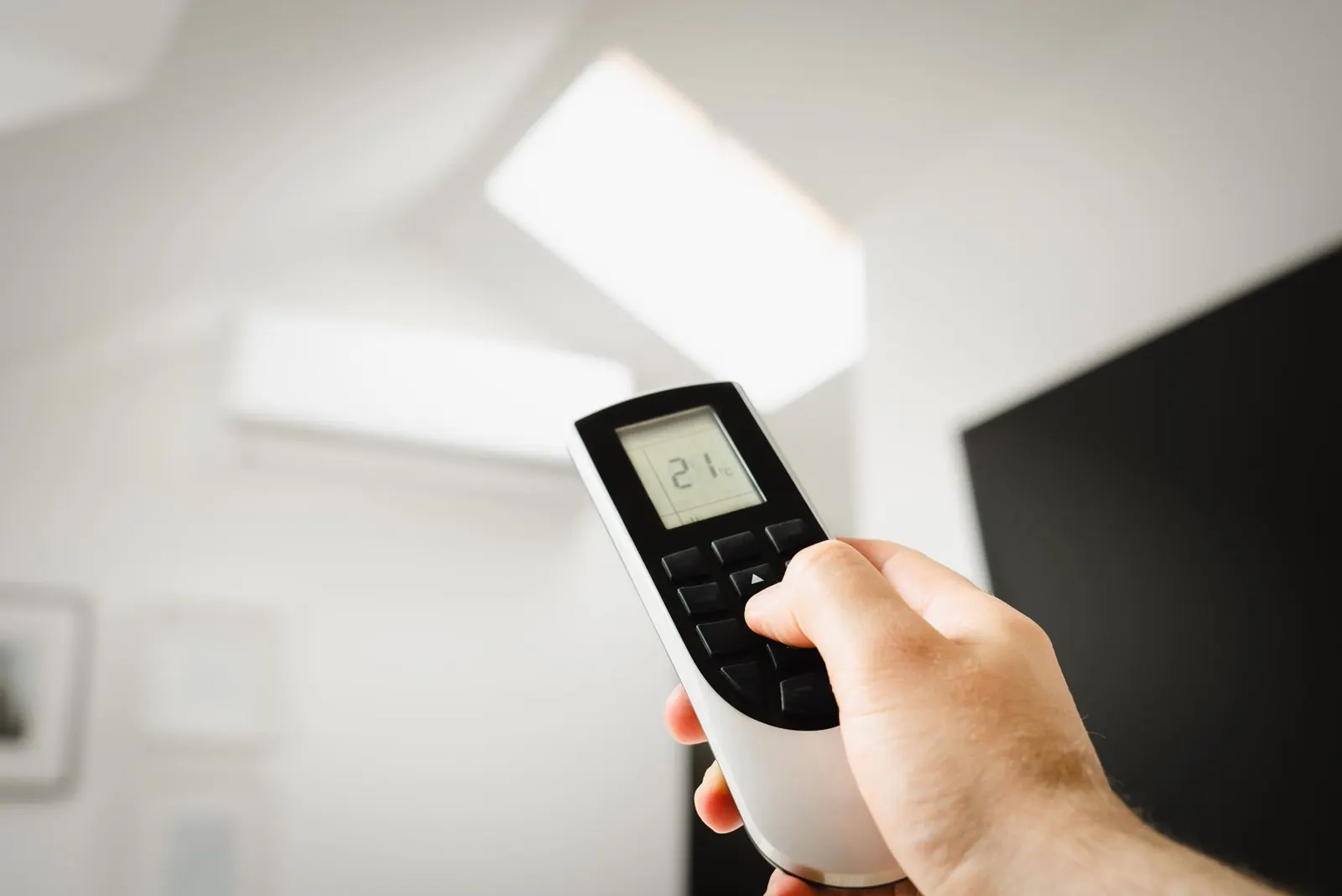 A hand holding an air conditioning remote control set to 21 degrees
